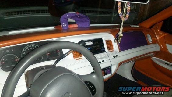 Interior of a car with orange and white trim, purple accents, and a gray steering wheel. A purple baseball cap sits on the dashboard