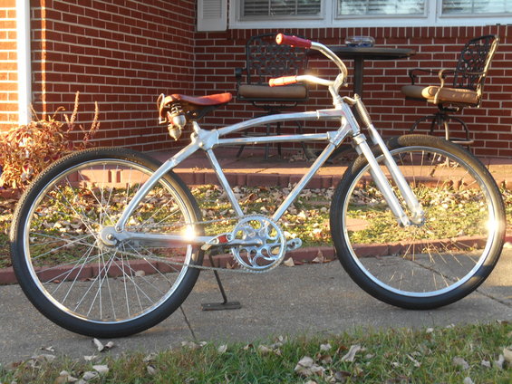 Chrome cruiser bicycle with red handlebars and a brown leather seat, parked on a sidewalk