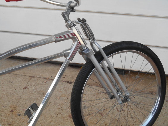 Close-up of a vintage bicycle's front fork and wheel. It has a chrome frame and red handlebars