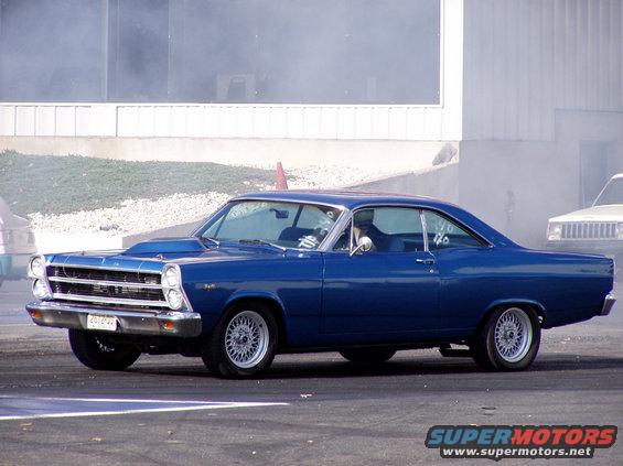 Blue 1966 Ford Fairlane coupe with a scoop on the hood, seen from the side at a drag strip
