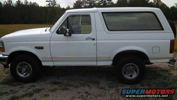 White Ford Bronco SUV, side view, parked on gravel with trees in background