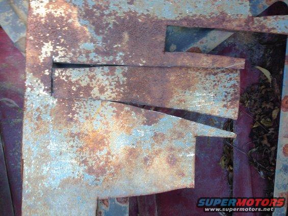Rusted metal panels with cutouts, showing red undercoating and some debris