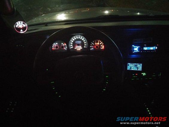 2000 Mercury Grand Marquis interior at night, showing illuminated dashboard gauges, steering wheel, and aftermarket radio