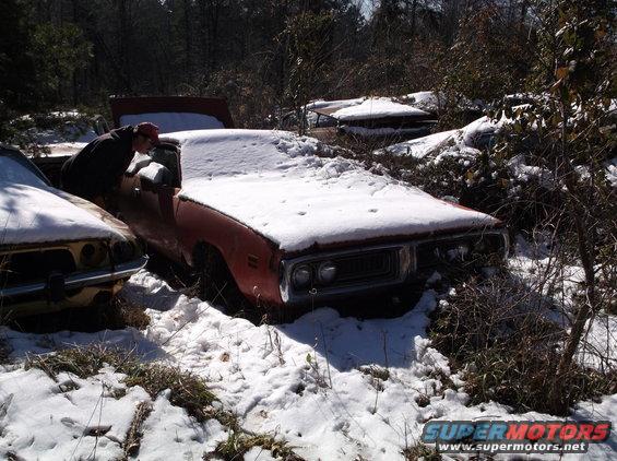 guy looking into a snow-covered 1973 Dodge Charger in a junkyard