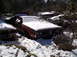 1974 Dodge Challenger - A person inspects a snow-covered 1973 Dodge Charger among other abandoned vehicles in a wooded area.