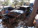 1974 Dodge Challenger - A heavily rusted car sits in a junkyard, partially covered in snow, with trees growing around it.