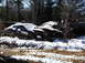 1974 Dodge Challenger - Two abandoned cars sit in a snowy wooded area, showing significant damage.