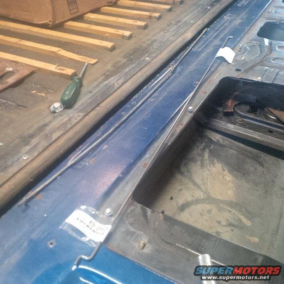 Blue vehicle interior floor with a screwdriver and some wooden planks in the background. A small plastic bag with a label is attached to the blue panel