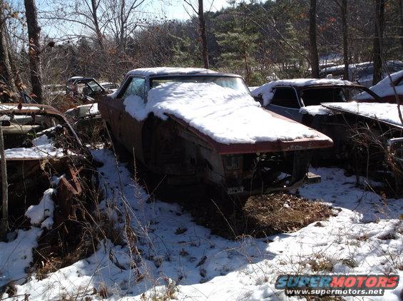 Abandoned car covered in snow in a junkyard with other vehicles visible