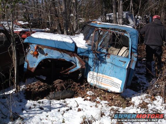 Rusty blue truck cab with Harley-Davidson decal in snowy junkyard.