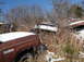 1974 Dodge Challenger - Several old vehicles sit abandoned in a snowy, overgrown junkyard under a clear blue sky.