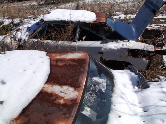 Two rusty, snow-covered vintage cars parked in a field.
