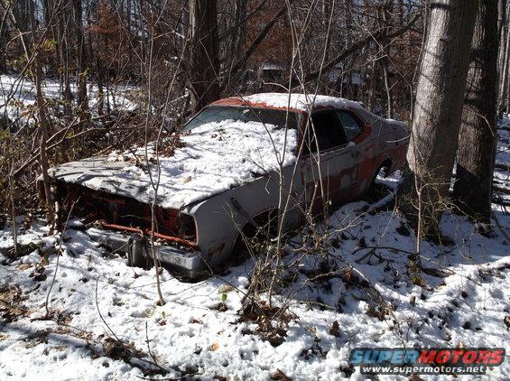 Abandoned 1974 Dodge Challenger covered in snow in a wooded area.
