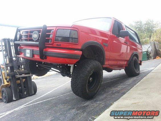 Red 1995 Ford Bronco lifted by a forklift, front 3/4 view