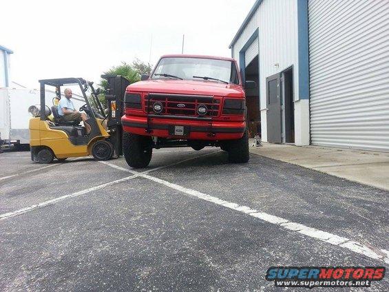 1995 Ford Bronco parked in front of a building with a forklift nearby