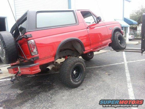 Red 1995 Ford Bronco lifted by a forklift, spare tire mounted on rear door