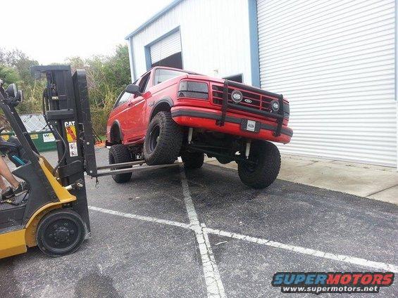 Red 1995 Ford Bronco with lifted suspension being moved by a forklift