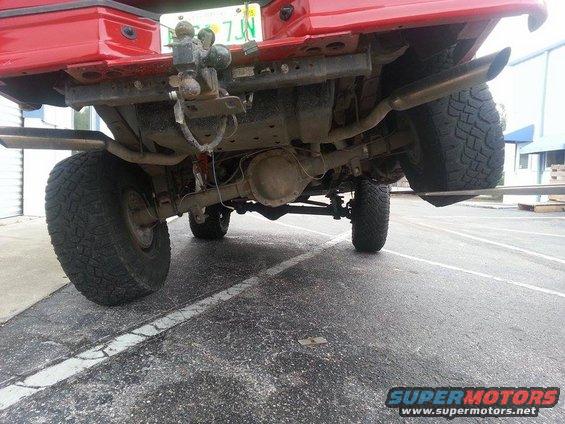 Rear axle, suspension, and exhaust of a red 1995 Ford Bronco. Tow hitch visible