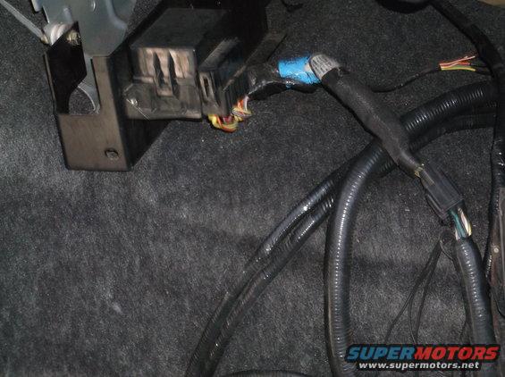 Automotive wiring harness and junction box with blue tape and connectors on gray carpet