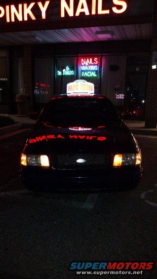 Dark sedan with Papa John's sign on roof, parked in front of Pinky Nails