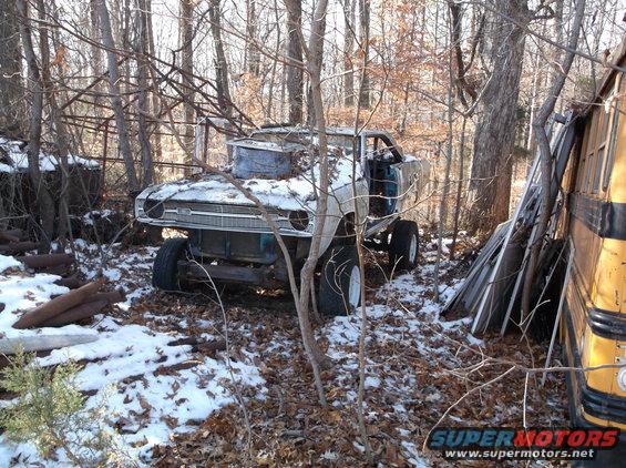 Modified lifted vehicle in woods with snow, next to a school bus.