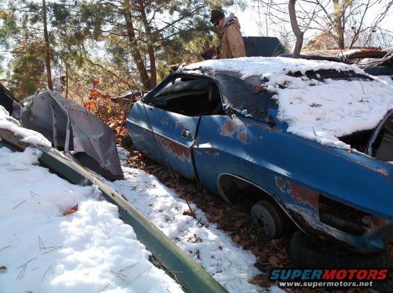 Blue classic car covered in snow and leaves, with a person standing nearby.