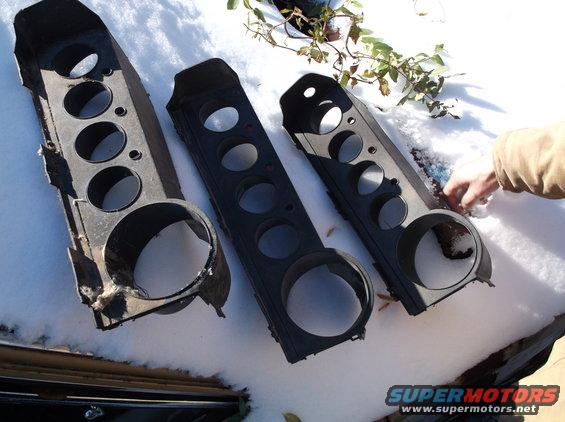 Three black plastic gauge cluster housings with circular cutouts on a snowy surface.