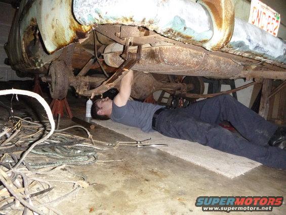 Rusty 1953 Plymouth Belvedere rear underside with a man working on the suspension