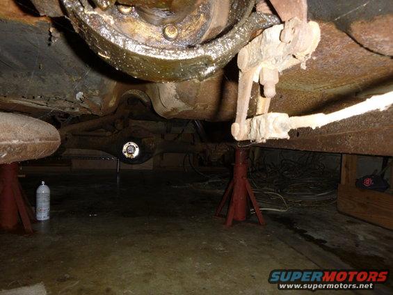 Underside of a vehicle on jack stands, showing rusty suspension and differential