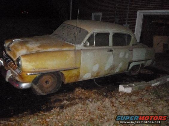 old sedan with primer spots on the side, parked outside at night