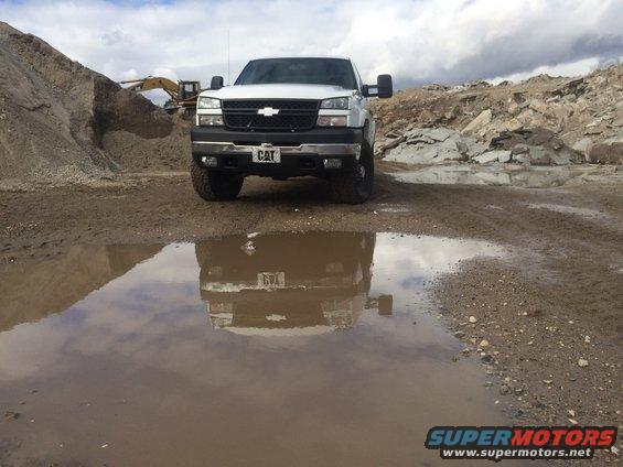 White Chevrolet Silverado pickup truck with a CAT license plate, parked in a quarry with a puddle reflection