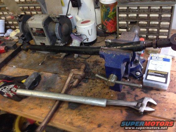 Workbench with a tie rod assembly in a vise, adjustable wrench, hammer, and grinder