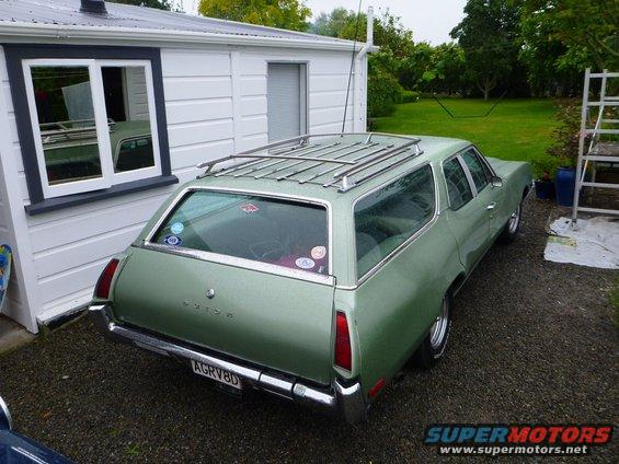 Green 1969 Lincoln Continental station wagon with a roof rack, parked next to a white house
