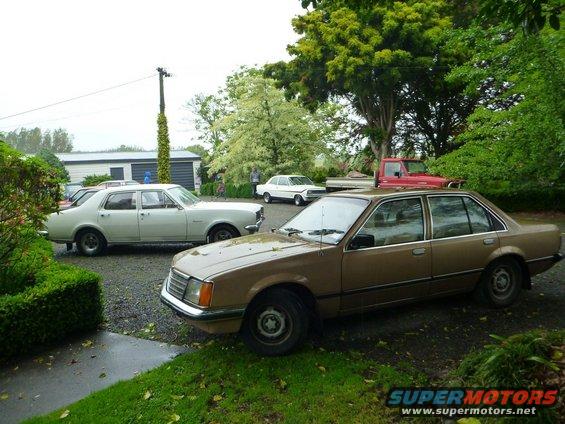 Several cars parked in a gravel driveway with a red truck in the background