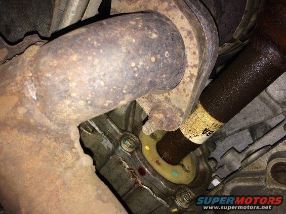 Close-up of driveshaft entering transmission housing with exhaust pipe flange nearby. Yellow and blue paint marks visible on housing