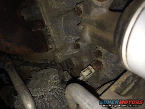 Close-up of a sensor plugged into an engine component, with bolts and metal tubing visible