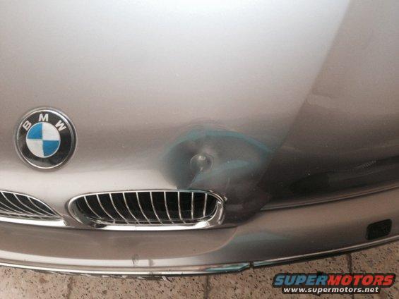 Silver BMW hood with a dent and blue paint transfer near the emblem and grille