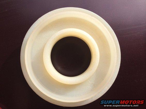 White plastic automotive part with concentric rings and a central hole, on a dark surface