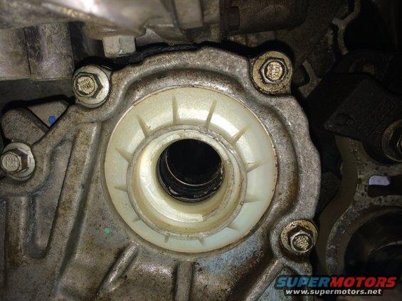 Close-up of a metal engine component with a white plastic seal and several bolts
