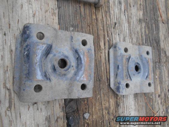Two dusty, gray metal brackets with four bolt holes each, lying on a wooden surface
