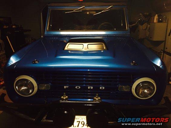 Blue Ford Bronco with a hood scoop and white trim around headlights. License plate visible