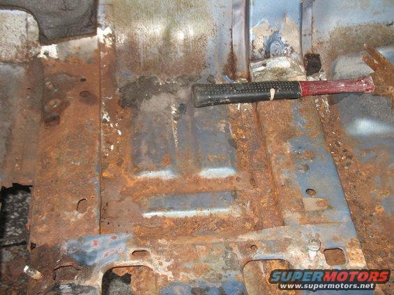 rusted out floor pan with a hammer resting on it