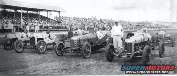 Race cars lined up with spectators in the background