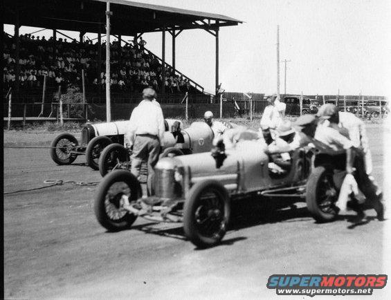 1909 Ford Model T race cars lined up at a track with spectators in bleachers