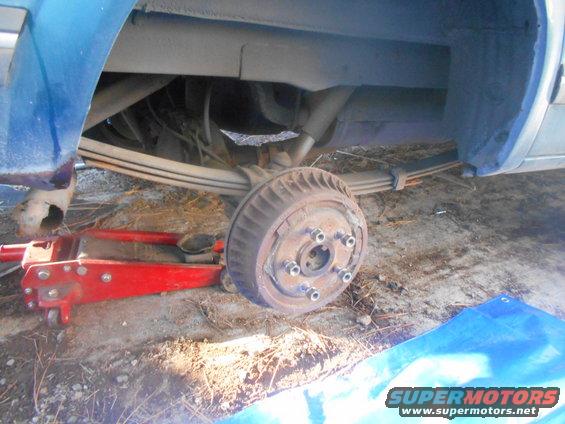 blue vehicle's rear axle and leaf springs are visible, with a drum brake and a red jack underneath