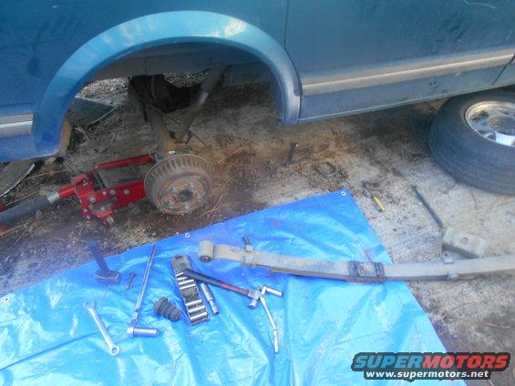 blue van with rear axle removed, jack under frame, tools and leaf spring on blue tarp