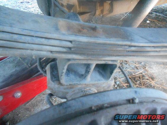 Close-up of a vehicle's leaf spring and suspension component, with a red jack visible