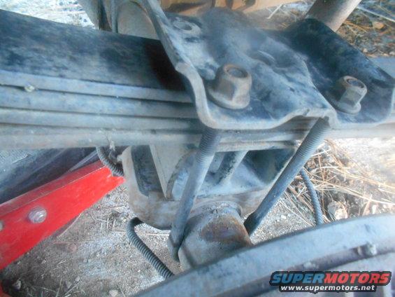 Rear leaf spring suspension with U-bolts and mounting bracket. A red jack is visible to the left