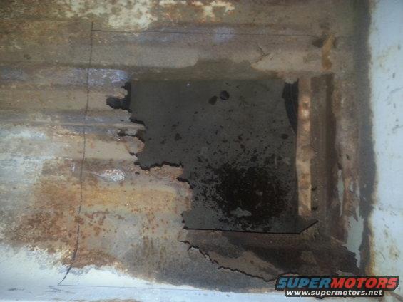 Rusted metal frame with a large hole showing dark interior. Some white paint is visible