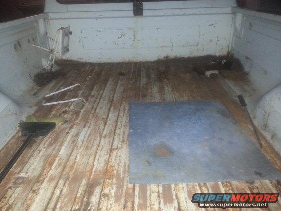 Interior of a dirty, weathered truck bed with wooden planks and a metal plate